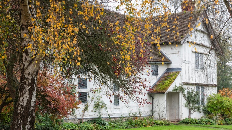 The manor house surrounded by autumnal leaves on the trees.